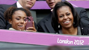 First lady Michelle Obama, right, smiles as former USA gymnast Dominique Dawes snaps a photo as they watch Serena Williams of the United States compete against Jelena Jankovic of Serbia at the All England Lawn Tennis Club in Wimbledon, London at the 2012 Summer Olympics, Saturday, July 28, 2012. (AP Photo/Elise Amendola)