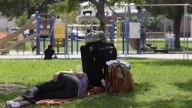 A homeless woman rests under a shade tree as children play at Lions park in Costa Mesa, Calif. October 2012. (AP Photo/Chris Carlson)