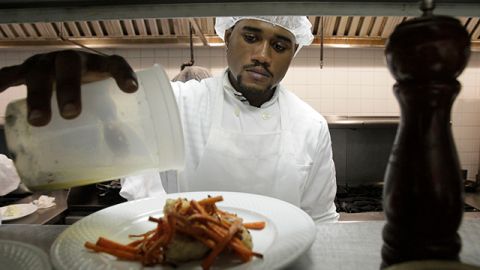 In this photo taken Oct. 18, 2011, Andrew McLeod, a student from the Colors Hospitality Opportunities Workers (CHOW) Institute, pours a lemon-caper sauce on a plate of monk fish and carrots as he works in the kitchen learning culinary arts skills at Colors Restaurant in New York. The restaurant-cooperative was founded by workers from the Windows of the World Restaurant, located in the World Trade Center, who survived the Sept. 11 attacks in 2001. (AP Photo/Kathy Willens)