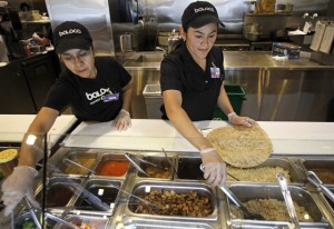Workers Maria Gaitan, left, and Ana Lopez, right, assemble burritos at a Boloco restaurant. (AP Photo/Steven Senne)