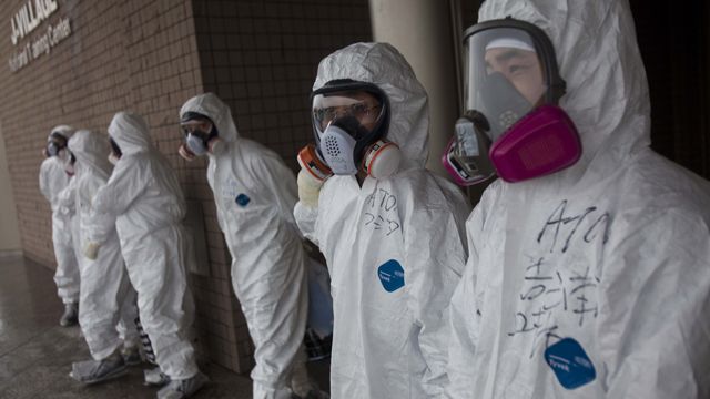 Workers dressed in protective suits and masks wait outside a building. (AP Photo/David Guttenfelder, Pool)