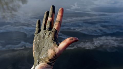 Hand covered with wet coal ash from the Dan River swirling in the background as state and federal environmental officials continued their investigations of a spill of coal ash into the river in Danville, Va., Wednesday, Feb. 5, 2014. Duke Energy estimates that up to 82,000 tons of ash has been released from a break in a 48-inch storm water pipe at the Dan River Power Plant in Eden N.C. on Sunday. (AP Photo/Gerry Broome)