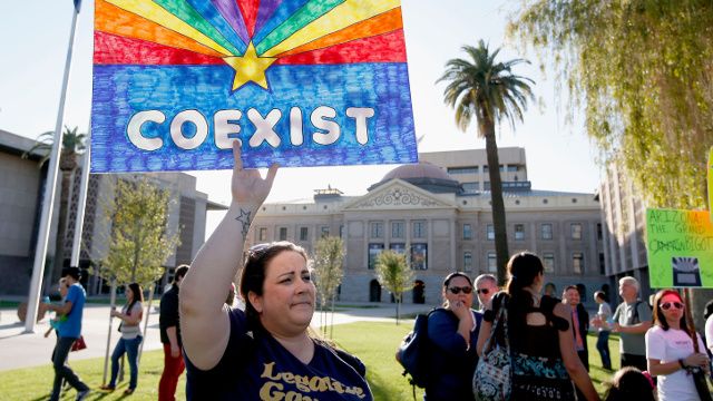 Jo Beaudry holds up a sign as she joins nearly 250 gay rights supporters protesting SB1062 at the Arizona Capitol, Friday, Feb. 21, 2014, in Phoenix. The protesters gathered demanding Gov. Jan Brewer veto legislation that would allow business owners to refuse to serve gays by citing their religious beliefs. (AP Photo/Ross D. Franklin)