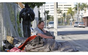 A homeless man sits on a sidewalk in Miami, Florida. (AP photo/ Alan Diaz.)