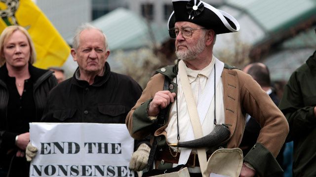 Mike Challenger, of Bothell, Wash., applauds a speaker as he stands dressed in Revolutionary-period wear at a tax day tea party rally of about a hundred protesters Friday, April 15, 2011, in Bellevue, Wash. (AP Photo/Elaine Thompson)