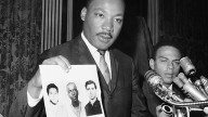 Dr. Martin Luther King displays pictures of three civil rights workers,who were slain in Mississippi the summer before, from left Michael Schwerner, James Chaney, and Andrew Goodman, at a news conference in New York. (AP Photo/JL, File)
