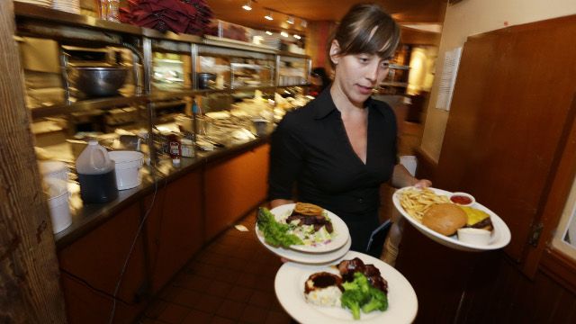 In this June 2, 2014 photo, Wendy Harrison, a waitress at the icon Grill in Seattle, carries food to a table as she works during lunchtime. An Associated Press comparison of the cost of living at several other major U.S. cities found that a $15 minimum wage, like Seattle adopted this week, will make a difference, but won’t buy a lavish lifestyle. (AP Photo/Ted S. Warren)