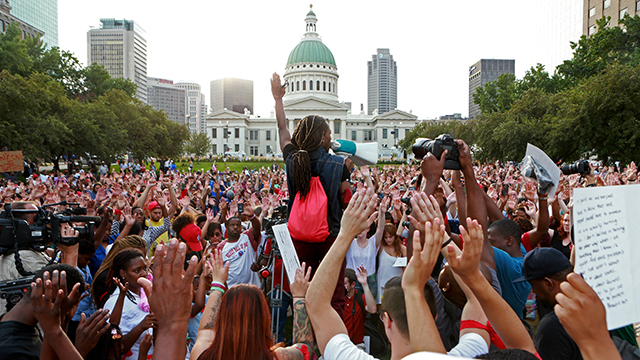 Jay Mitchell, of Pagedale, Mo., speaks and solicits a response of hands in the air from the crowd Thursday, Aug. 14, 2014, in St. Louis during a peace vigil and moment of silence for Michael Brown, an unarmed teenager who was shot and killed by Ferguson, Mo., police Saturday. Vigils have been held across the country for people who died at the hands of police. (AP Photo/St. Louis Post-Dispatch, Christian Gooden)