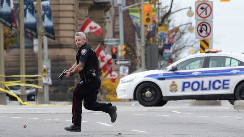 An Ottawa police officer runs with his weapon drawn outside Parliament Hill in Ottawa on Wednesday Oct. 22, 2014. A soldier standing guard at the National War Memorial was shot by an unknown gunman and people reported hearing gunfire inside the halls of Parliament. Prime Minister Stephen Harper was rushed away from Parliament Hill to an undisclosed location, according to officials. (AP Photo/The Canadian Press, Sean Kilpatrick)