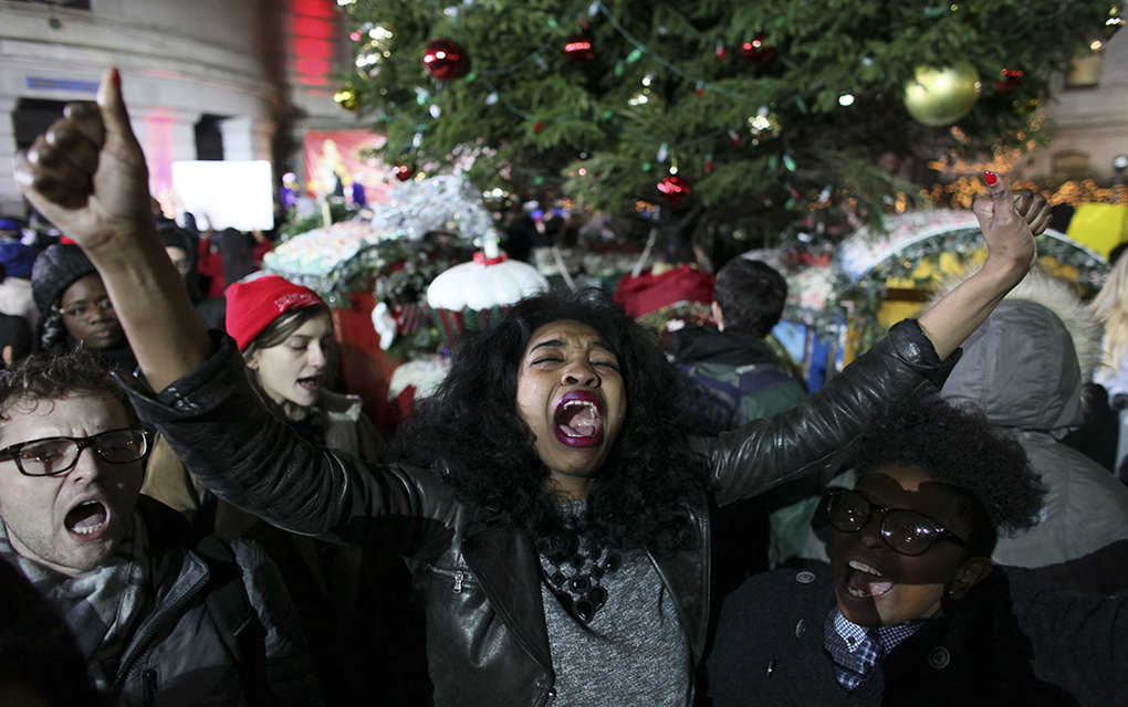 Angelica Simmons, center, holds her arms up in the air while participating in a demonstration at a tree lighting ceremony, Wednesday Dec. 3, 2014, in Philadelphia. The crowd, protesting the deaths of two unarmed black men at the hands of police, rallied at the train station and marched through downtown before disrupting a tree lighting ceremony at City Hall. (AP Photo/ Joseph Kaczmarek)
