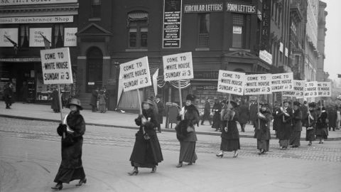 A line of suffragists march with banners that read "Come to the White House Sunday at 3," in Washington DC in 1915. (Photo by Harris & Ewing/Buyenlarge/Getty Images)