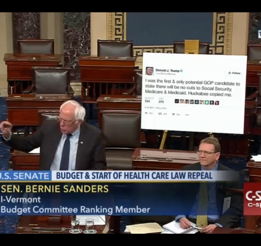 Bernie Sanders displays a poster of one of Donald Trump's tweets from May 2015, reading “I was the first & only potential GOP candidate to state there will be no cuts to Social Security, Medicare & Medicaid. Huckabee copied me.”