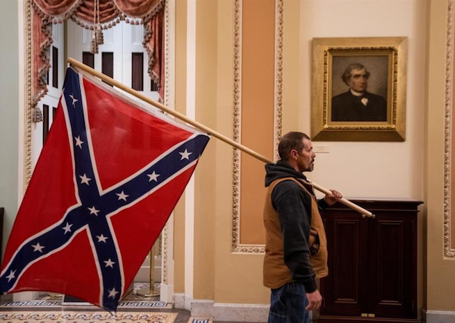 A member of the mob involved in the insurrection at the US Capitol on Wednesday, Jan. 6, 2021, holds a Confederate flag. (Source: Twitter)
